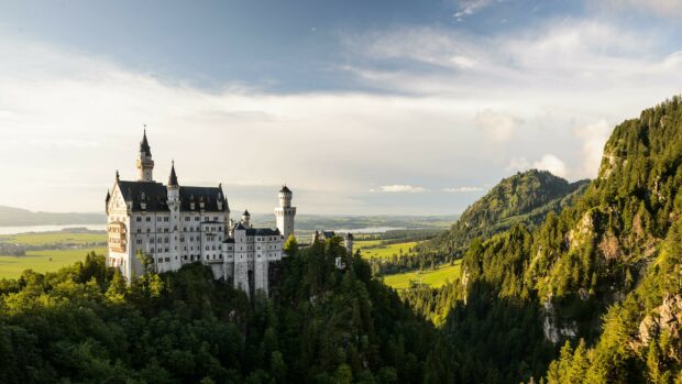 A stunning view of Neuschwanstein Castle surrounded by dense forest and mountains, 4K Desktop Wallpaper