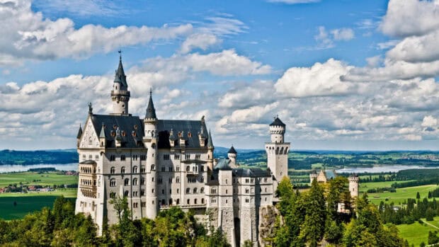 Neuschwanstein Castle stands majestically surrounded by green fields and blue skies, 2K Desktop Wallpaper