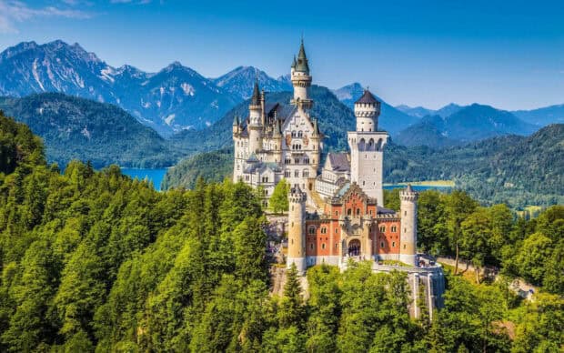 A scenic view of Neuschwanstein Castle surrounded by green forests and mountains, HD Desktop Wallpaper