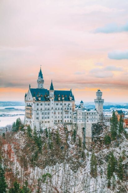 Neuschwanstein Castle stands majestically surrounded by snow covered trees at sunset, HD Mobile Wallpaper