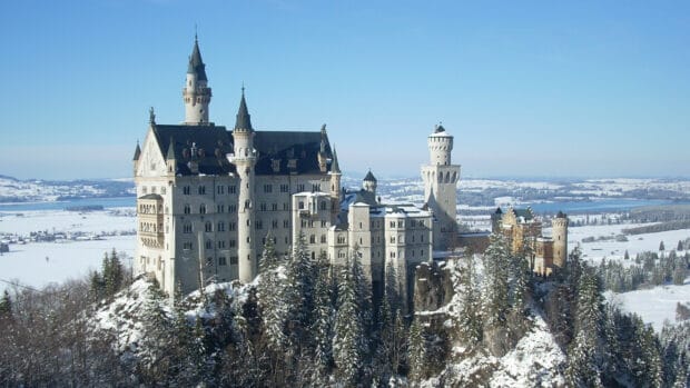 The Neuschwanstein Castle stands surrounded by snow covered trees and hills, 2K Desktop Wallpaper
