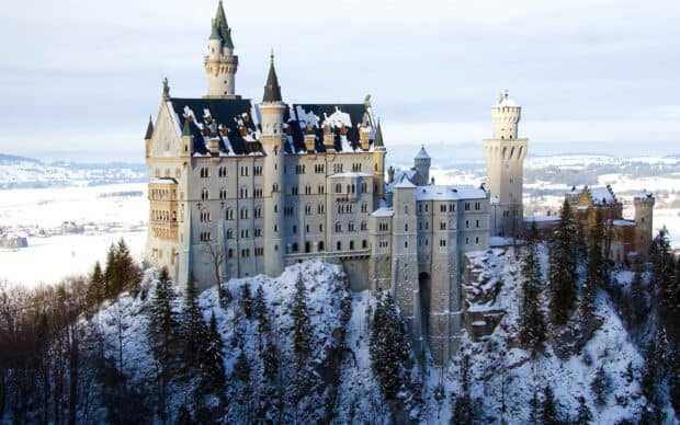 The Neuschwanstein Castle stands surrounded by snow covered trees and mountains, 2K Desktop Wallpaper