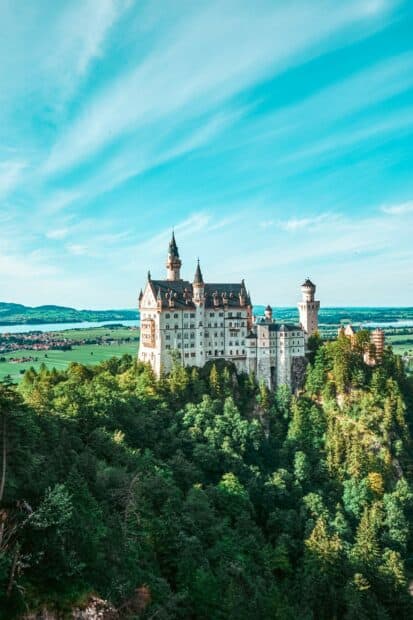 A stunning view of Neuschwanstein Castle surrounded by lush forest and clear sky, 2K Mobile Wallpaper