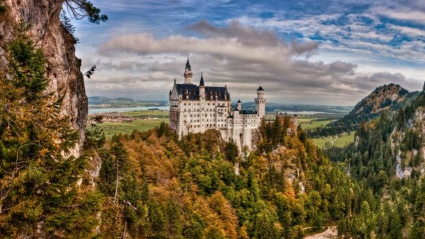 Neuschwanstein Castle stands above the colorful forest under a cloudy sky, 2K Desktop Wallpaper