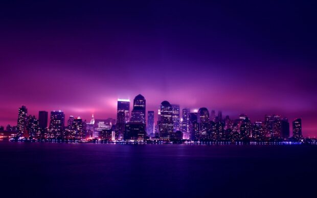 The New York skyline is illuminated with purple and pink lights under a cloudy night sky, 2K Desktop Wallpaper