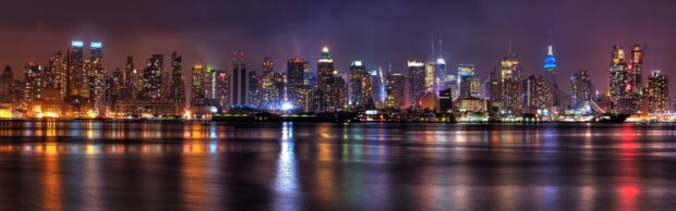 The New York skyline shows illuminated buildings reflecting on water at night, 4K Desktop Wallpaper