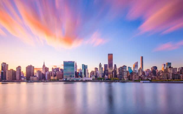 The New York skyline captures colorful clouds over calm water in the evening, 2K Desktop Wallpaper