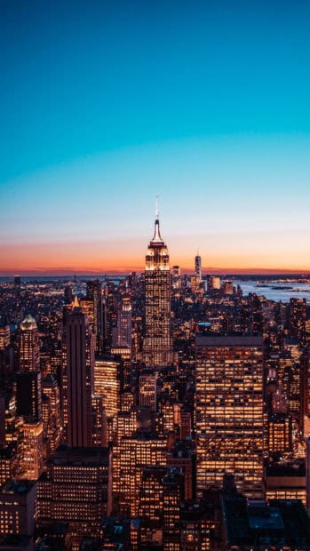 The New York skyline shows a vibrant cityscape lit up at sunset with iconic buildings, 4K Phone Wallpaper