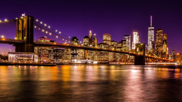 The New York skyline features bright city lights and a glowing bridge reflecting on the water at night, 4K Desktop Wallpaper