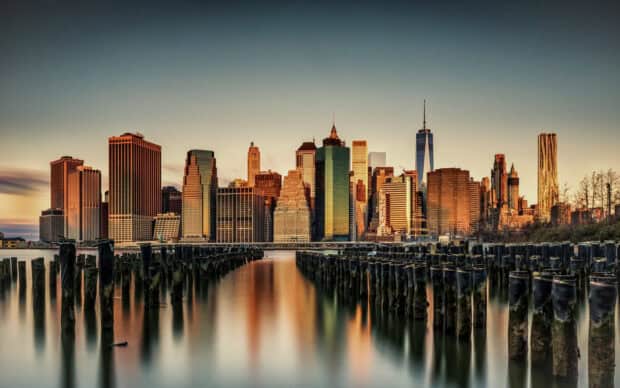 A beautiful view of New York skyline at sunset with wooden pillars in the water, HD Desktop Wallpaper