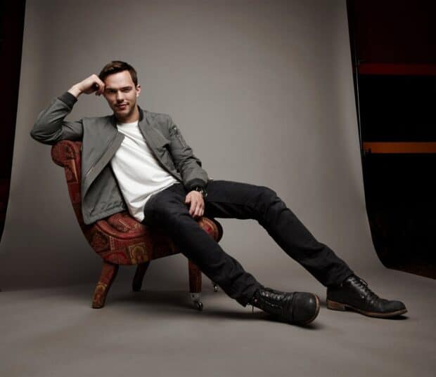 Nicholas Hoult posing casually while seated on a vintage patterned chair in a studio, HD Desktop Wallpaper