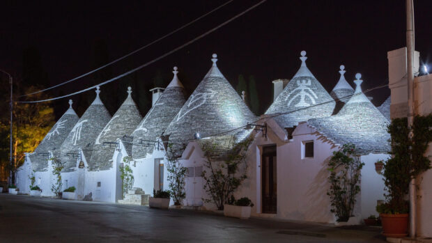 The night scene shows Alberobello houses with conical roofs under the dark sky, HD Desktop Wallpaper