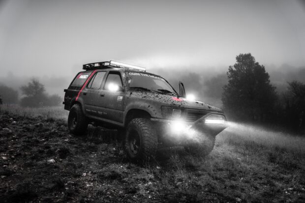 A rugged vehicle is engaged in off road driving with bright lights in a misty landscape, 2K Desktop Wallpaper