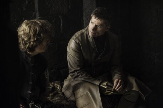 Nikolaj Coster Waldau is seated wearing a leather outfit with a golden hand in a dark room, 2K Desktop Wallpaper