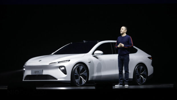 A person stands beside a white Nio Auto electric car on a dark stage during a presentation, HD Desktop Wallpaper