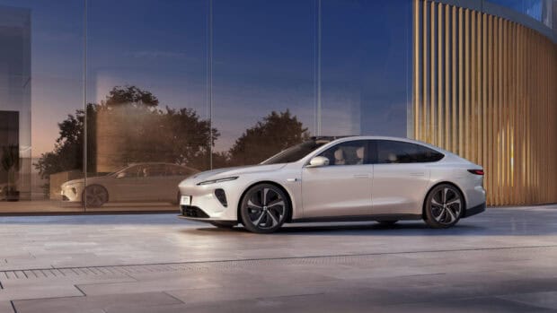 A sleek Nio auto is parked outside a modern glass building at dusk, 2K Desktop Wallpaper