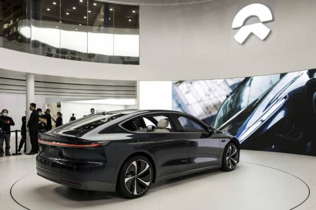 A sleek black Nio Auto is showcased indoors with people observing and a large brand logo in view, 2K Desktop Wallpaper