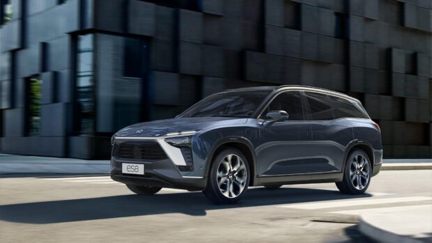 A sleek blue Nio auto is driving past a modern building in the city, 4K Desktop Wallpaper