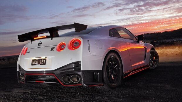 A white Nissan GT R is parked with glowing taillights under a vibrant sunset sky, HD Desktop Wallpaper