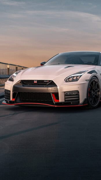 The Nissan GT R is parked on a road during sunset, showing its front design clearly, 4K Mobile Wallpaper
