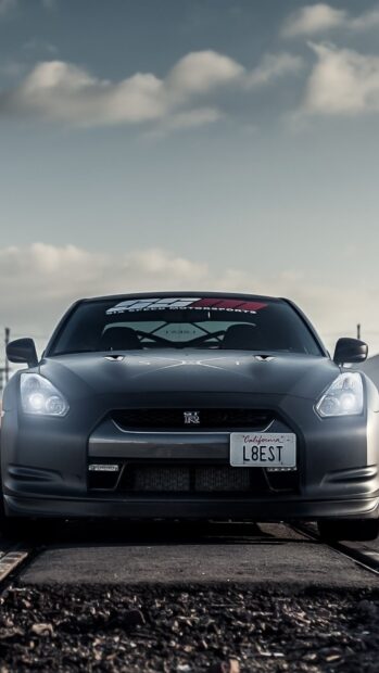 A Nissan GT R is parked on railway tracks under a cloudy sky, HD Mobile Wallpaper