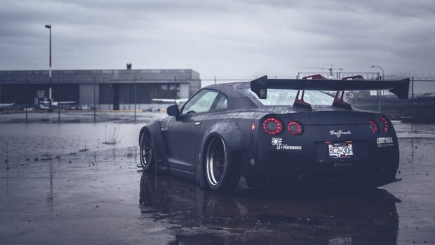 A Nissan GT R is parked on a wet surface with visible raindrops and industrial background, 4K Desktop Wallpaper