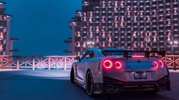 A Nissan GT R is parked with glowing taillights in front of a lit building at night, 4K Desktop Wallpaper