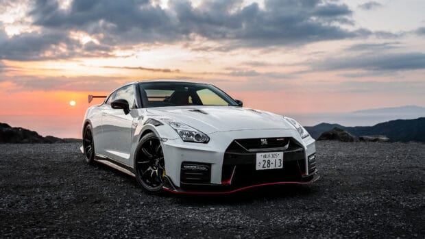 A white Nissan GT R parked on gravel with a scenic sunset sky and mountains behind, HD Desktop Wallpaper