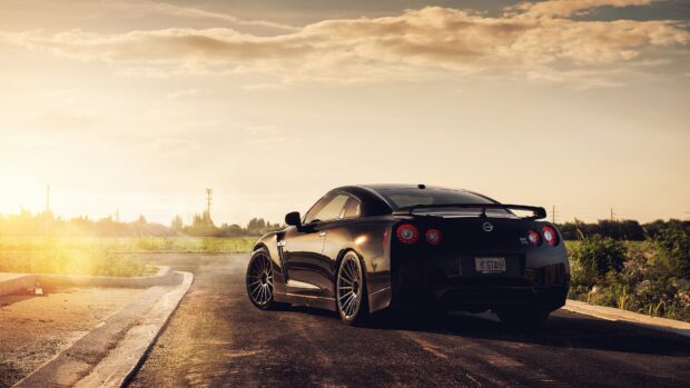 A black Nissan GT R is parked on a rural road with the sun setting in the background, 4K Desktop Wallpaper