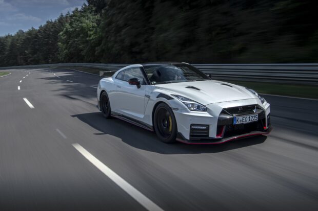 A white Nissan GT R is driving fast on a curved race track surrounded by trees, 2K Desktop Wallpaper