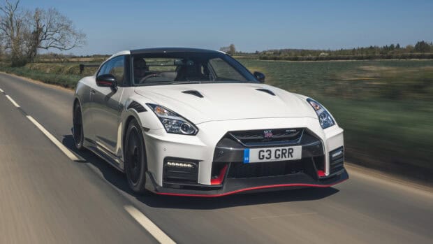A white Nissan GT R is driving fast on a rural road with clear skies and green fields, 2K Desktop Wallpaper
