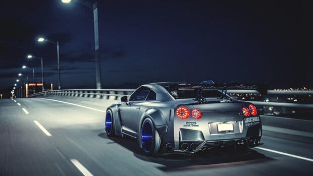 A Nissan GT R is driving fast on a bridge with city lights in the background, 4K Desktop Wallpaper