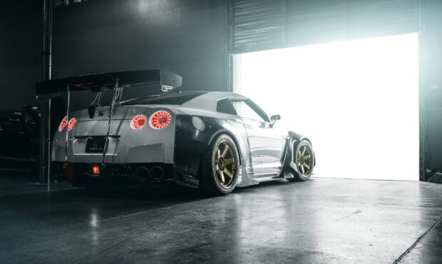 A Nissan GT R with gold rims is parked in a dim garage near an open bright door, HD Desktop Wallpaper