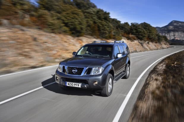 A Nissan Pathfinder driving quickly along a curved mountain road surrounded by trees and rocks, 2K Desktop Wallpaper