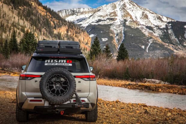 A Nissan Pathfinder is parked near a river with mountains in the background, 2K Desktop Wallpaper