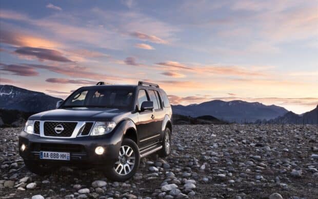 A Nissan Pathfinder parked on rocky terrain with mountains under a sunset sky, HD Desktop Wallpaper