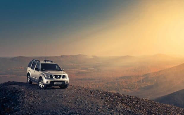 A Nissan Pathfinder is parked on a rocky mountain ridge under a clear sky at sunset, HD Desktop Wallpaper