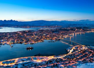 A scenic view of Norway city lights glowing at twilight over snowy landscape and water, 4K Desktop Wallpaper