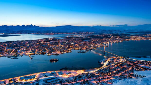 A scenic view of Norway city lights glowing at twilight over snowy landscape and water, 4K Desktop Wallpaper