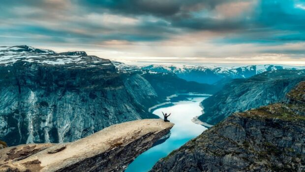 A person enjoys the breathtaking Norway fjord view while sitting on a cliff, HD Desktop Wallpaper