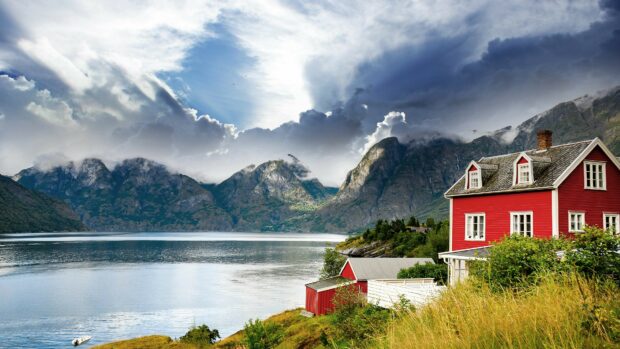 A red house by the water with mountains under cloudy skies in Norway Wallpapers, 4K Desktop Wallpaper