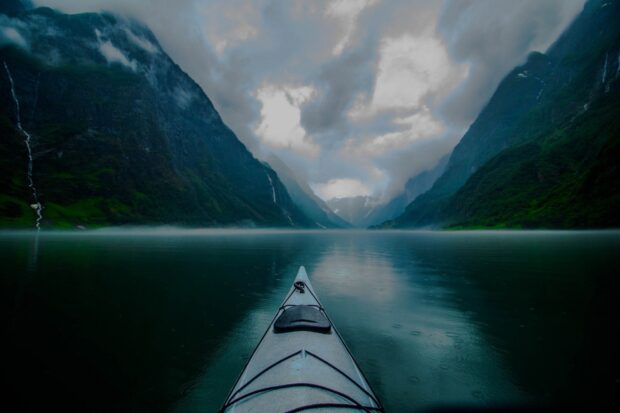 A kayak glides through the calm waters of the Norwegian fjords surrounded by misty mountains, HD Desktop Wallpaper