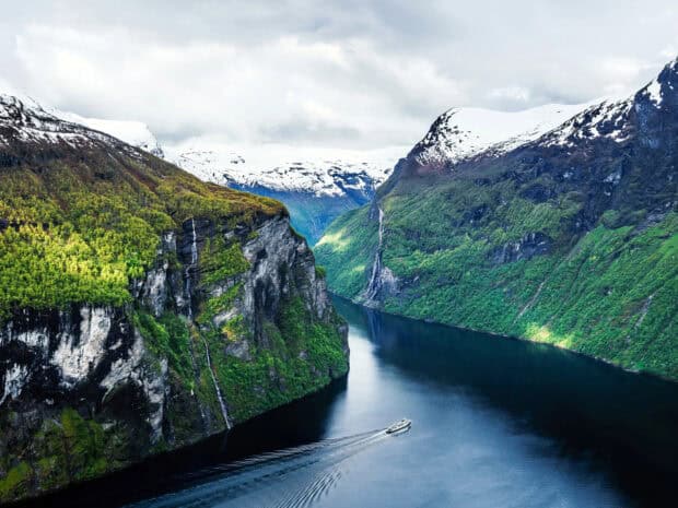 A boat sails through the deep Norwegian fjords surrounded by snow capped mountains, HD Desktop Wallpaper
