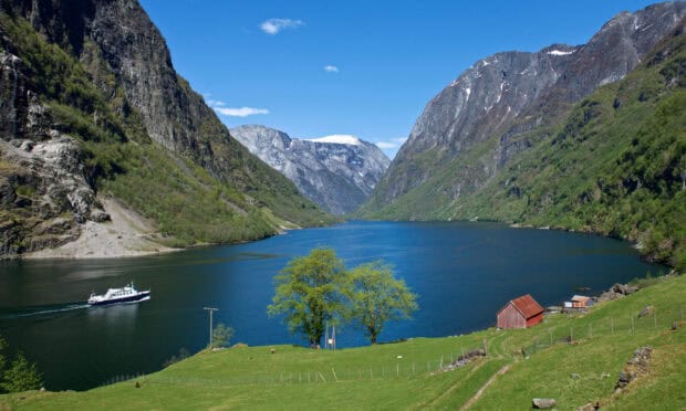 A boat sails through Norwegian fjords surrounded by mountains and green fields, HD Desktop Wallpaper