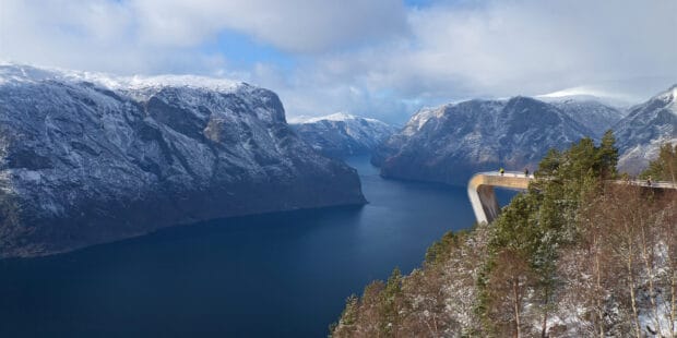 A scenic view of Norwegian fjords with snowy mountains and a fjord under a cloudy sky, 2K Desktop Wallpaper