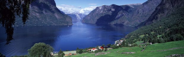 A scenic view of Norwegian fjords surrounded by green fields and mountains under a blue sky, 4K Desktop Wallpaper