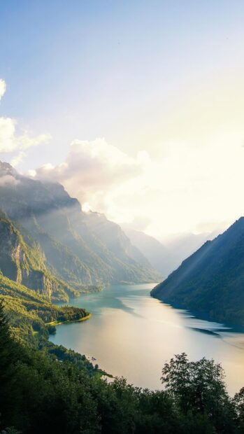 A serene view of Norwegian fjords with sunlight illuminating the mountain slopes and water, HD Phone Wallpaper