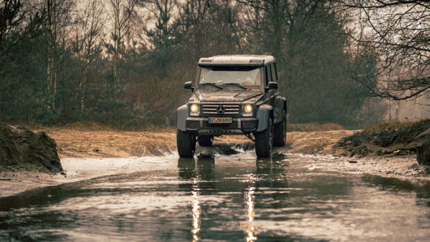 A rugged off road vehicle drives through a shallow water stream in a forest setting, 4K Desktop Wallpaper