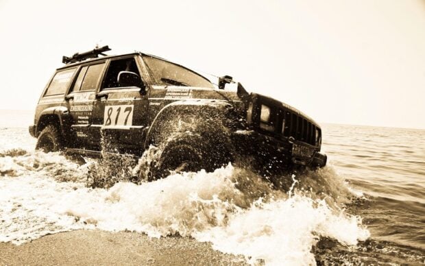 A rugged off road vehicle splashes through water on a beach during an adventurous drive, HD Desktop Wallpaper