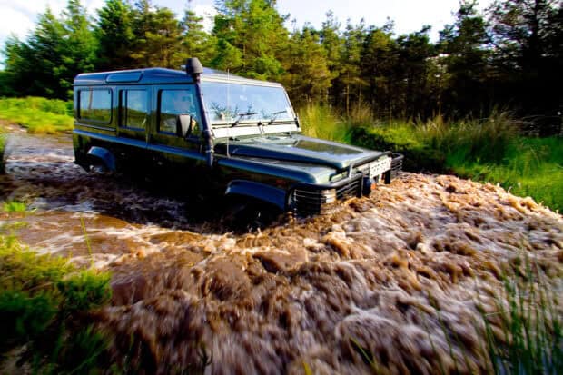 A rugged vehicle is driving through muddy water in a forest area, HD Desktop Wallpaper